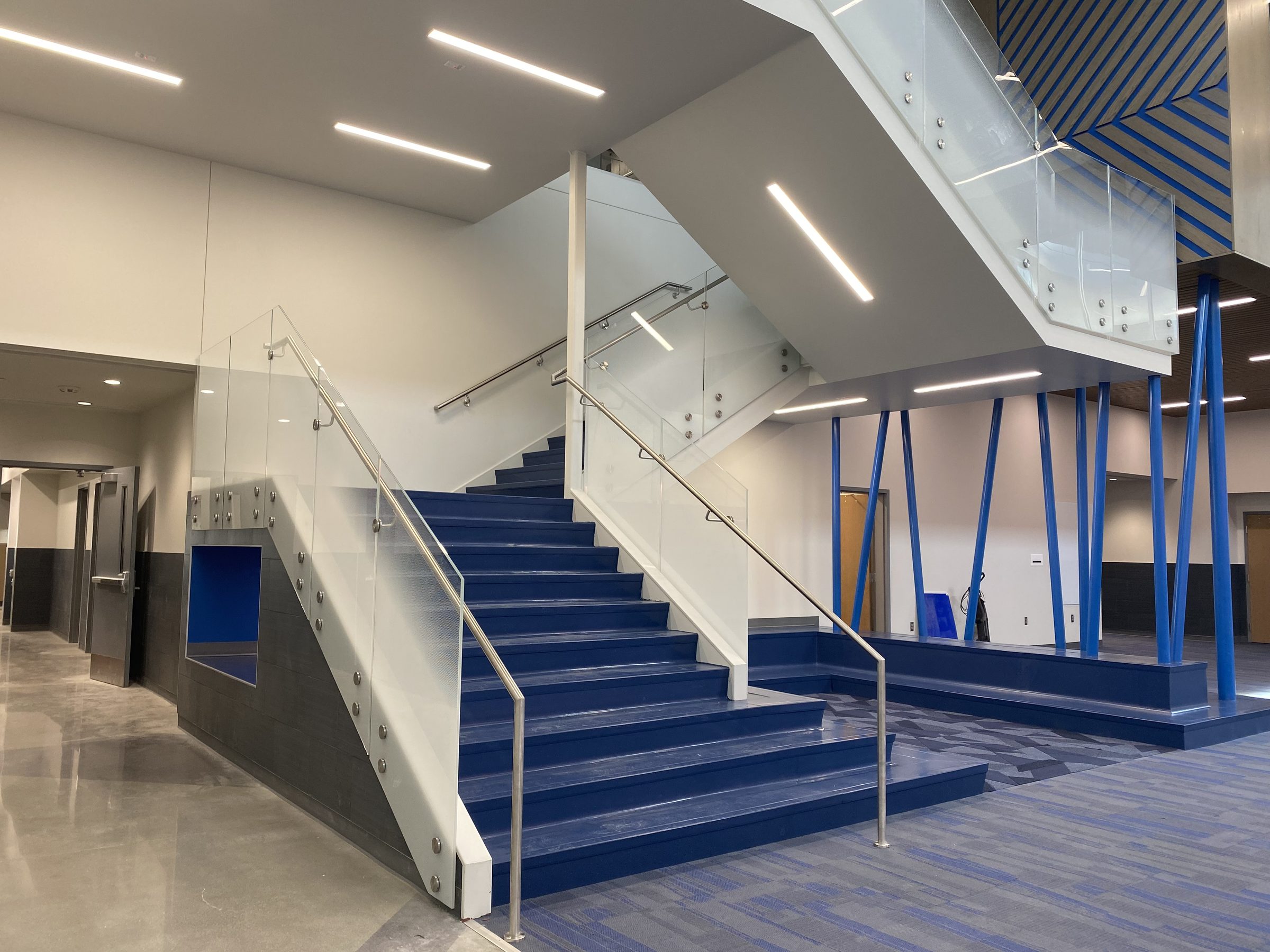 Glass guard fixed with exposed standoffs along a blue stair, with a stainless handrail, Blue Valley Schools