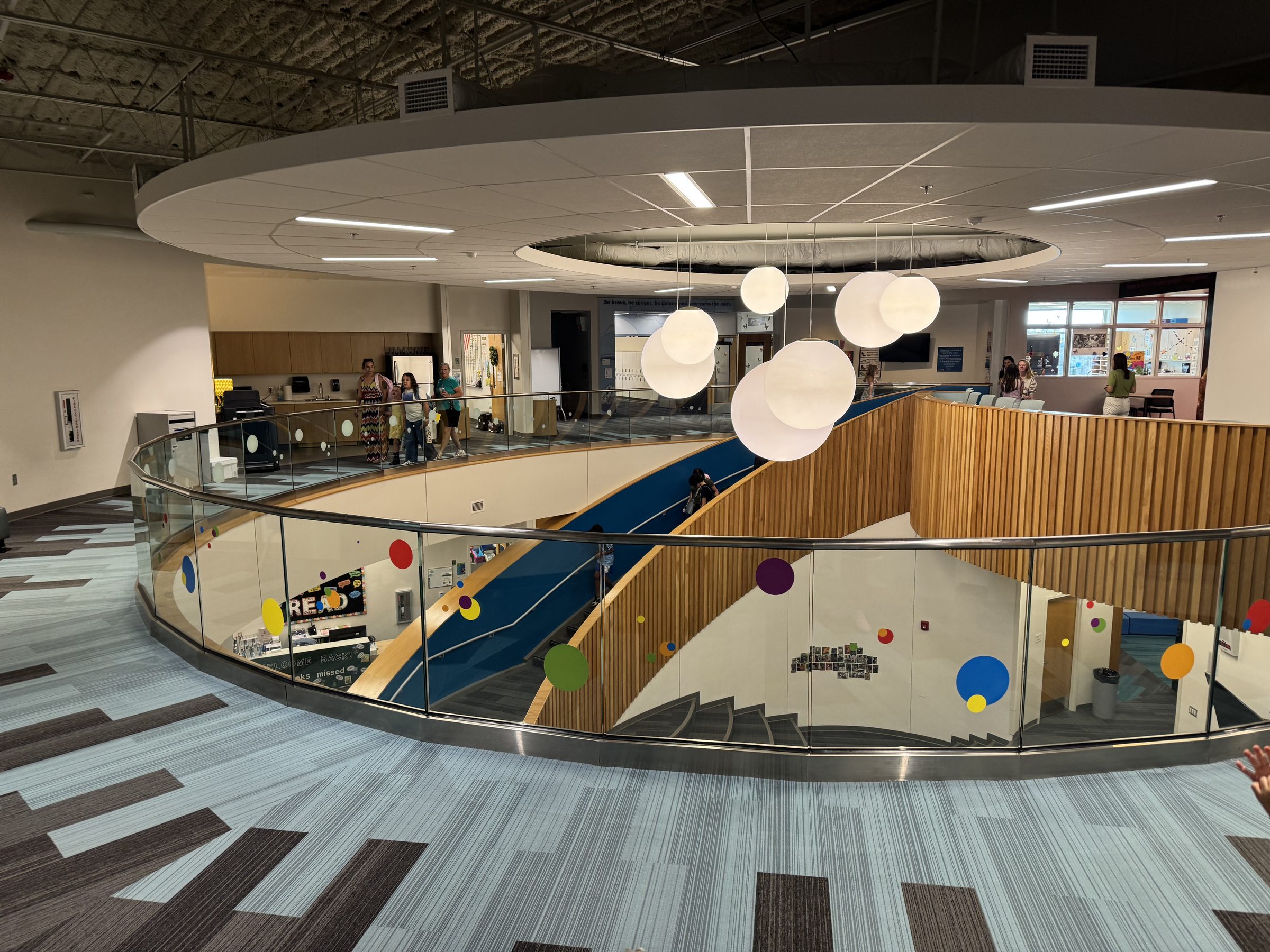 Curved glass guard around a mezzanine above a blue stair, NKC Rising Hill Elementary