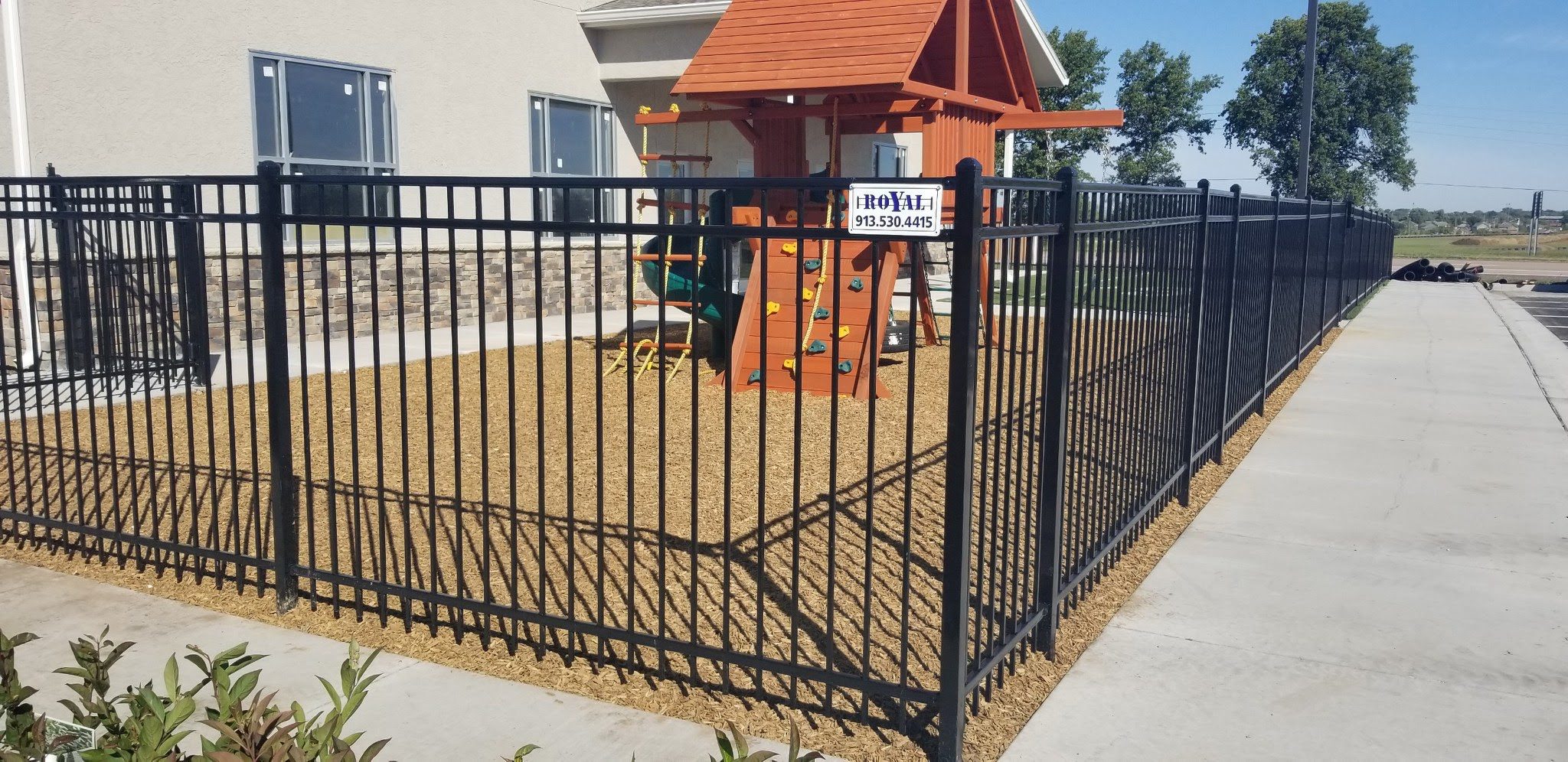 Black ornamental steel fence enclosing a play area beside a home