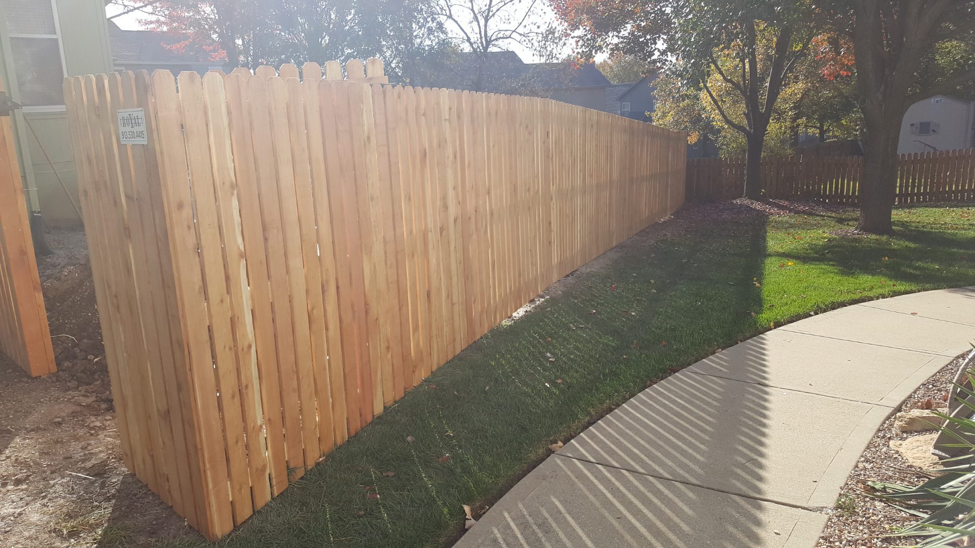 Six-foot spaced cedar fence with plain posts and wide pickets beside a sidewalk