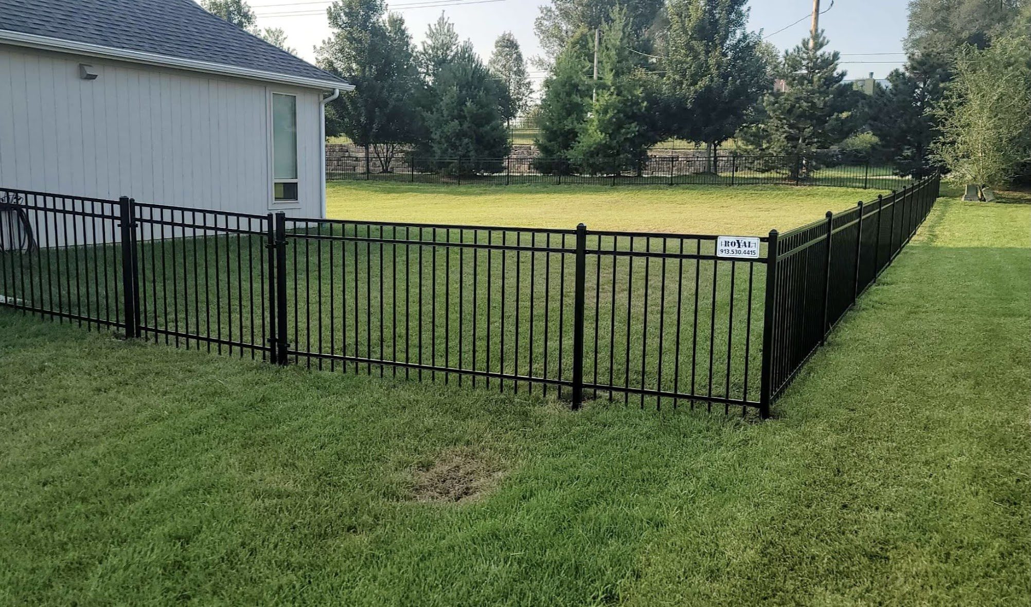Black ornamental steel fence enclosing a wide backyard lawn