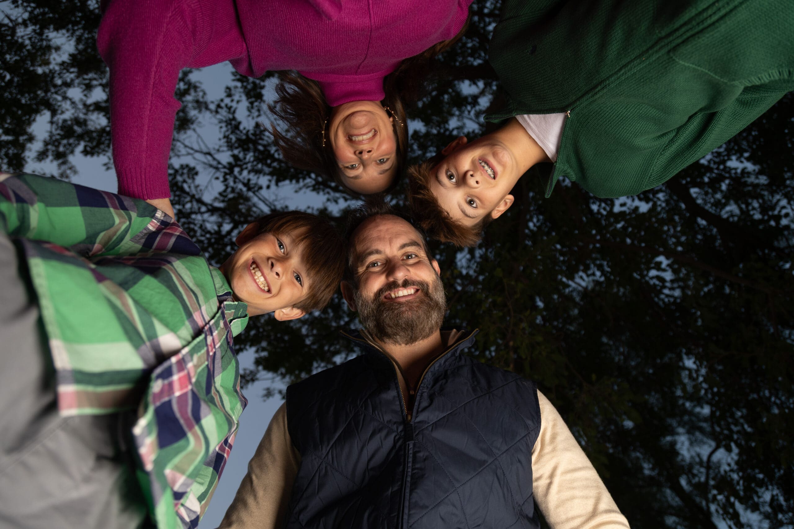 Smiling family of four photographed from below during an outdoor portrait session at English Landing Park in Parkville, Missouri.