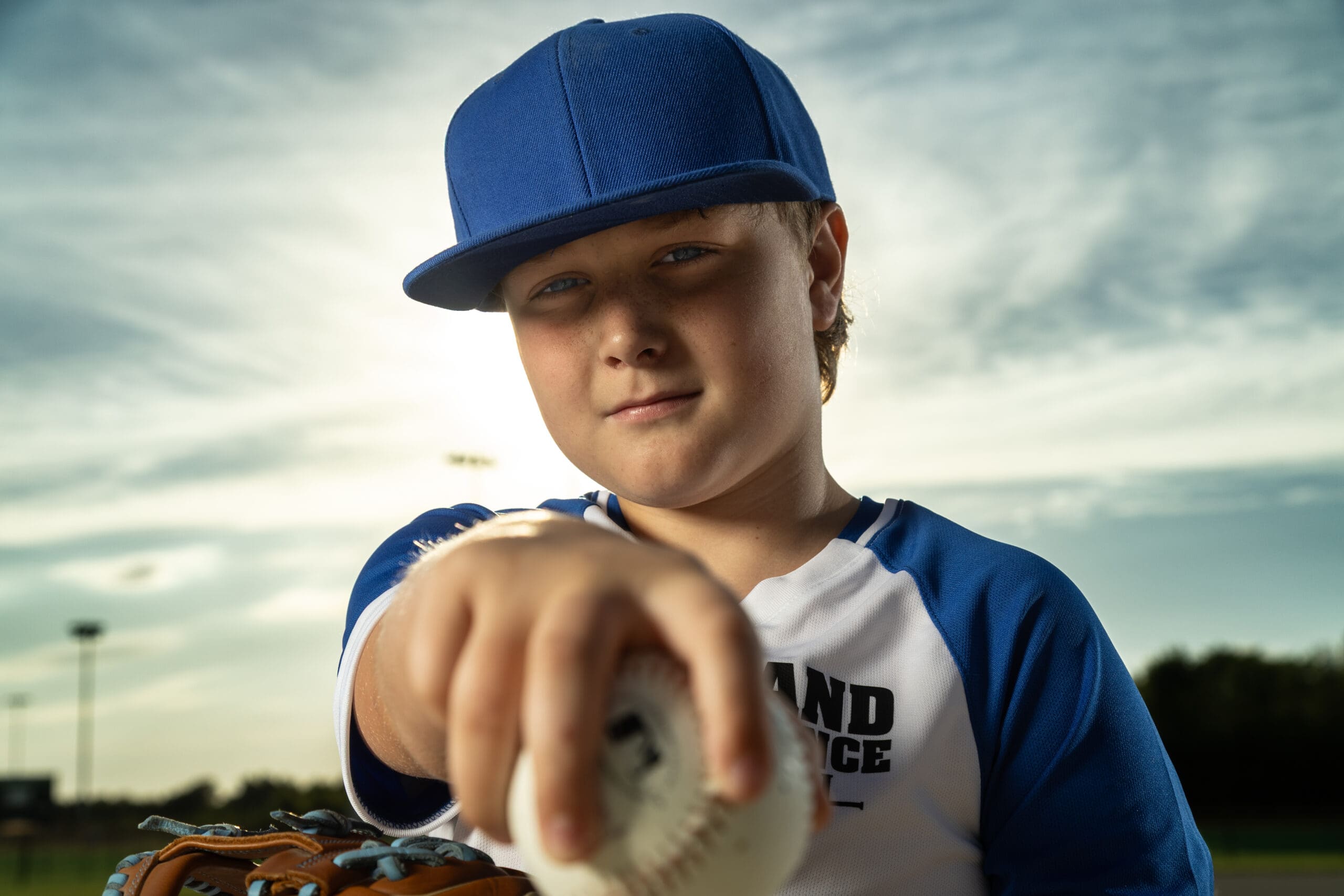 Kansas City Sports Photographer, Young baseball player pointing a baseball toward the camera during a dramatic outdoor sports portrait session in the Northland Kansas City.