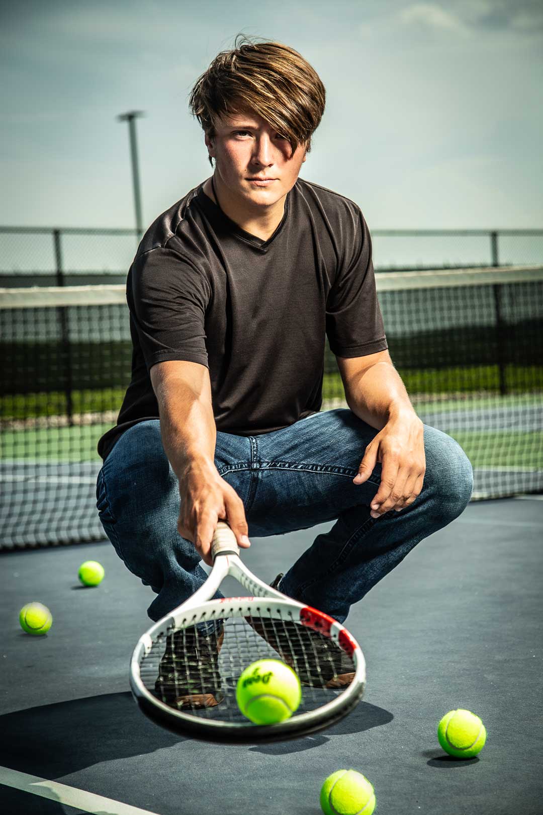High school senior tennis player posing with a tennis racket during a creative outdoor senior portrait session in Kansas City.