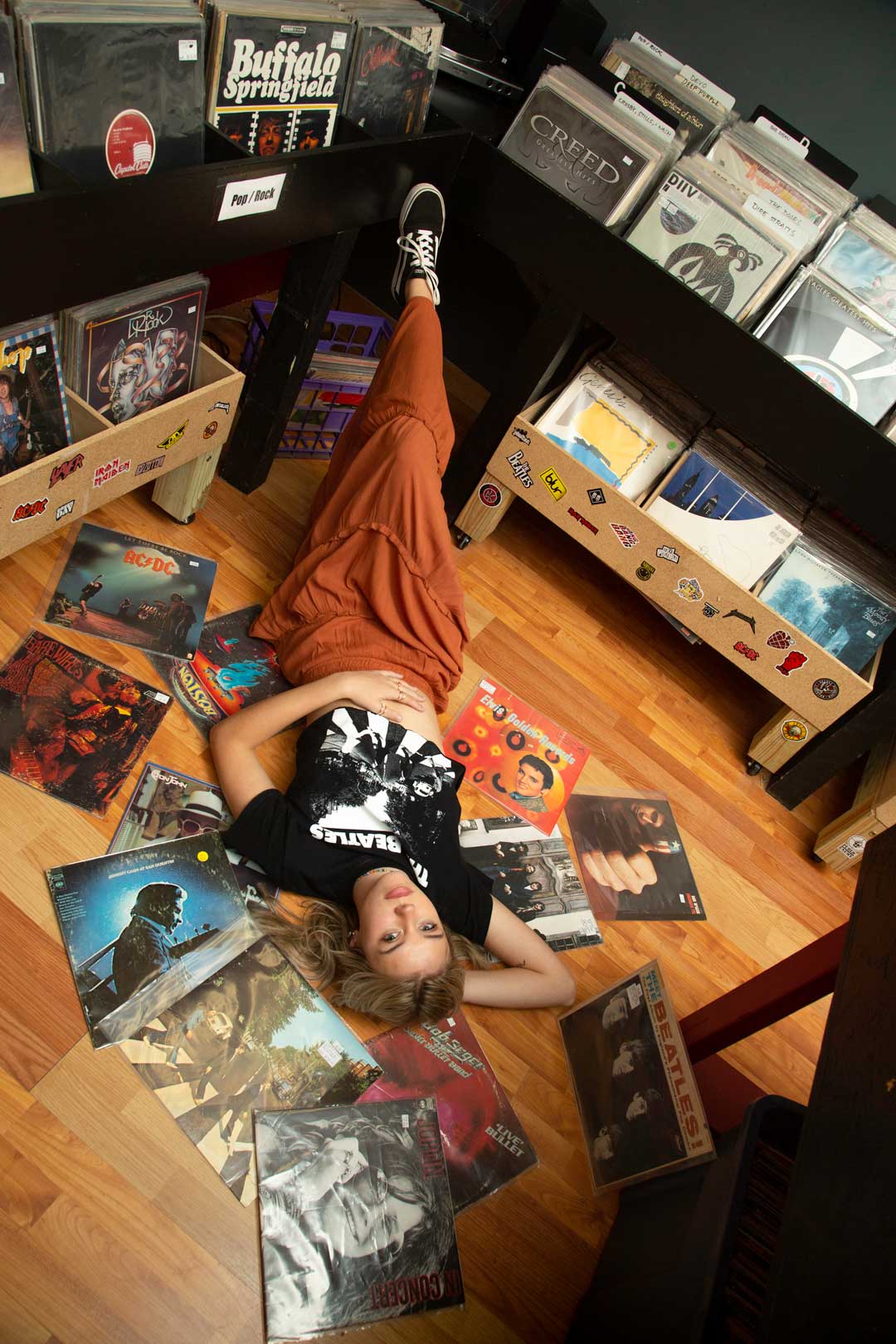 High school senior lying on the floor of a record store surrounded by classic rock vinyl albums, photographed by Gallery Portraiture.